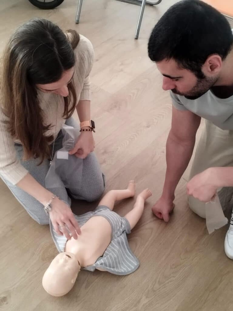 Padres practicando RCP con un muñeco de bebé en un curso de primeros auxilios