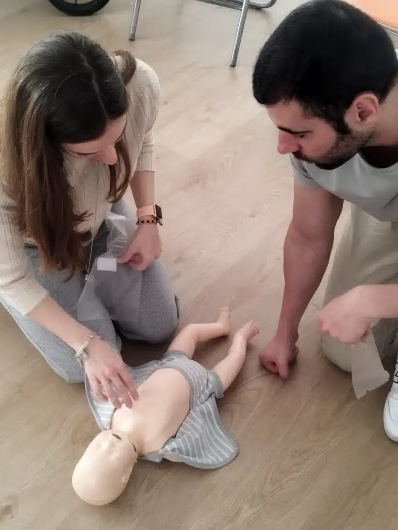 Pareja practicando RCP en un maniquí de bebé