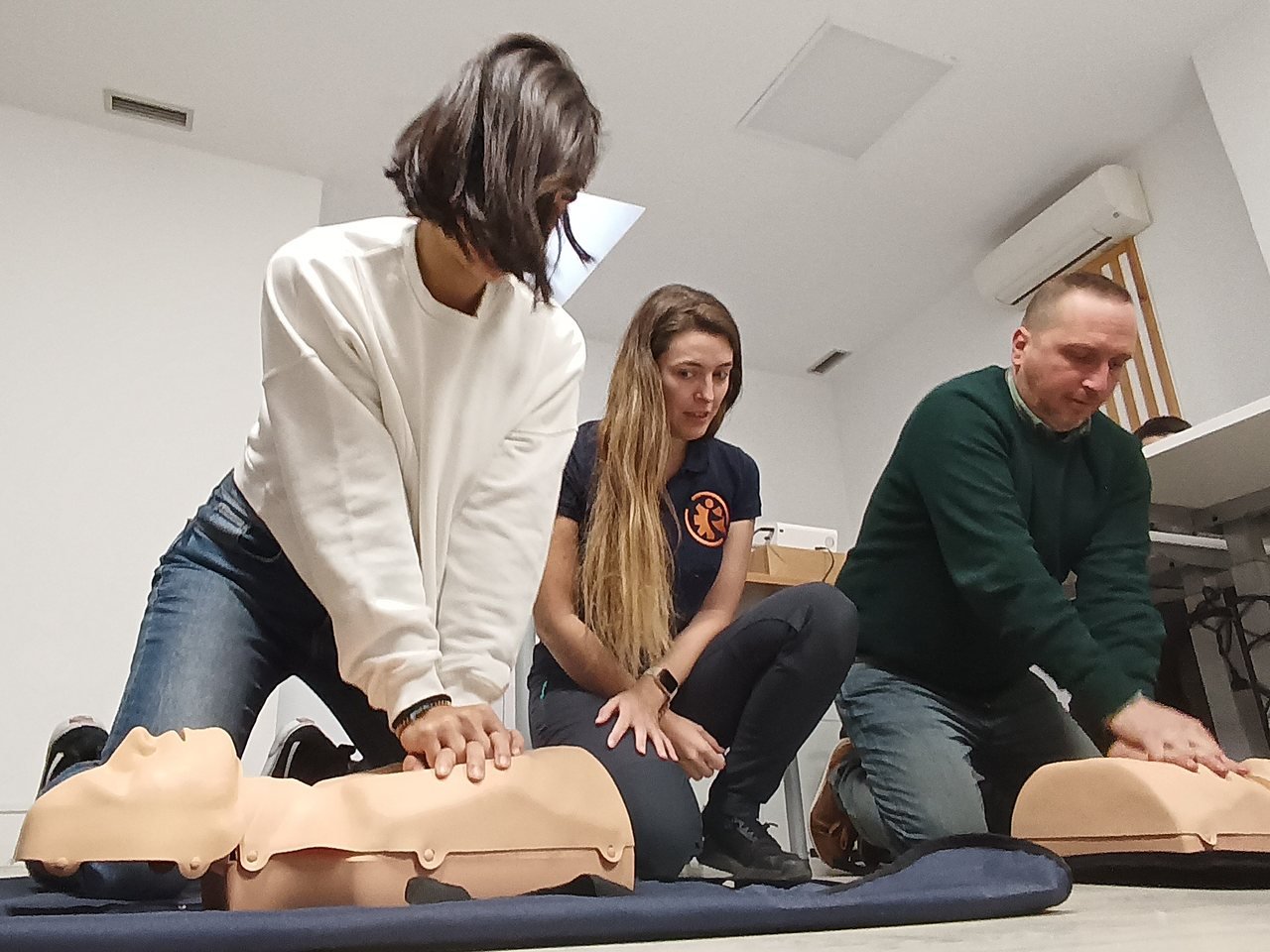 Alumnos practicando compresiones toracicas de RCP sobre maniquies con una instructora de Salvar Vidas en un curso de SVB y DESA
